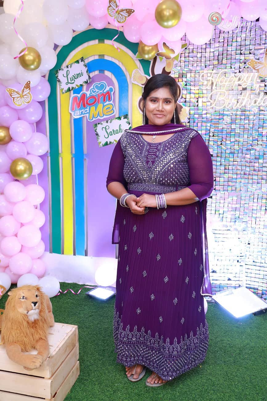 Sarah's mom in a stunning purple dress at the birthday celebration backdrop, captured by Lollipop Photography
