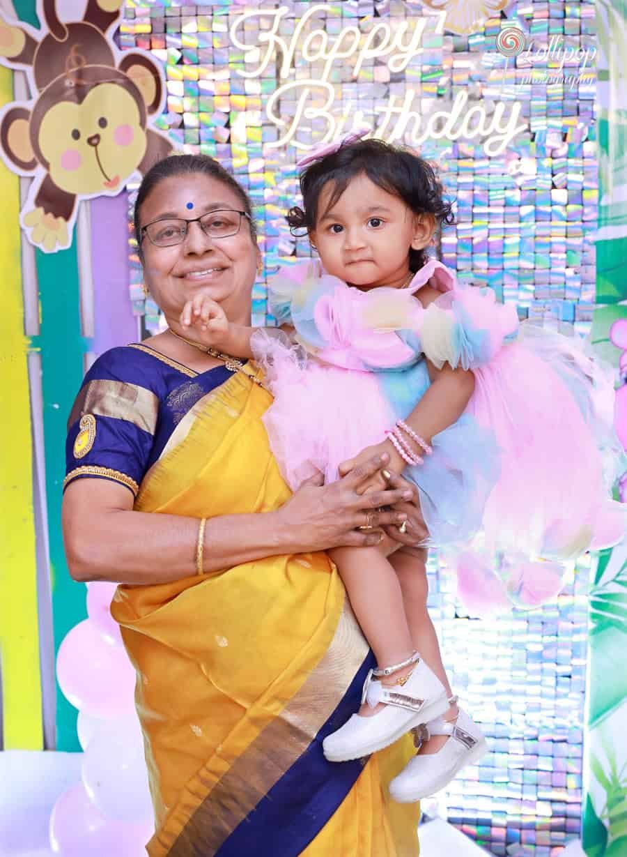Sarah held by her grandmother against a colorful birthday background, captured by Lollipop Photography