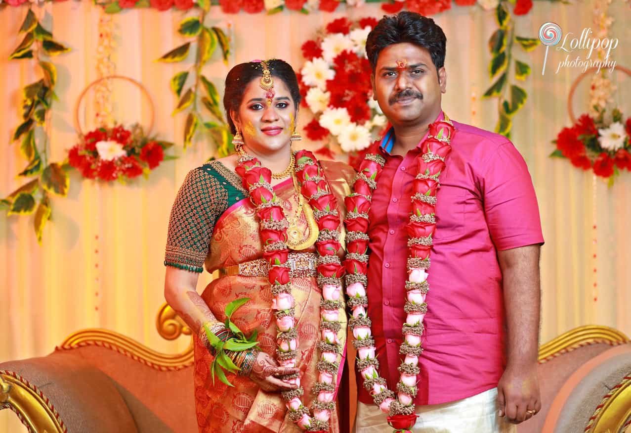 The happy couple stands in front of a beautiful floral backdrop, celebrating their baby shower with elegance in Chennai, captured by Lollipop Photography