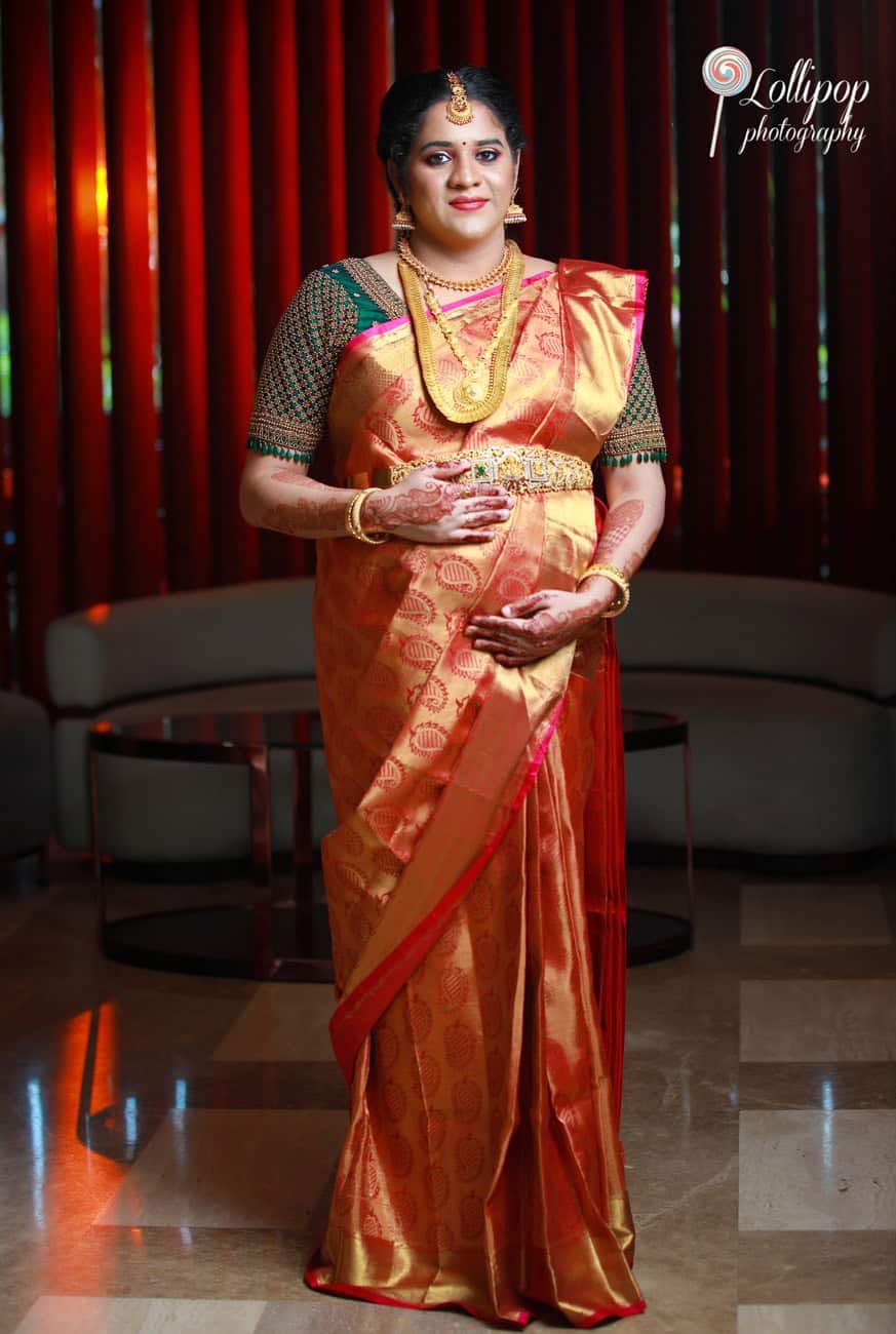 An elegant portrait of an expecting couple, both dressed in traditional attire, with the mother-to-be radiating in her golden sari, captured by Lollipop Photography.