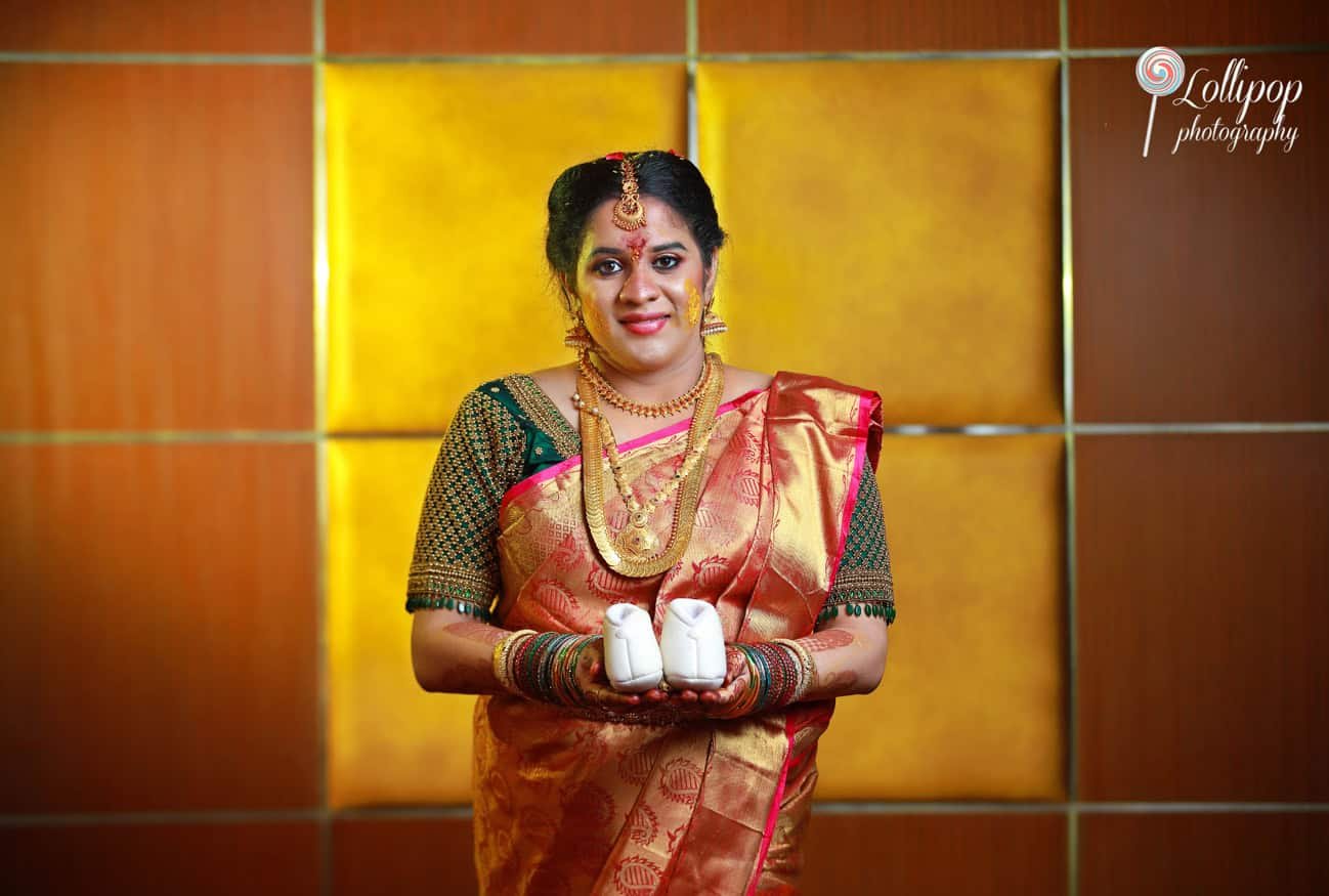 Hemalatha holding adorable baby shoes, symbolizing the excitement of welcoming a new life, beautifully photographed by Lollipop Photography