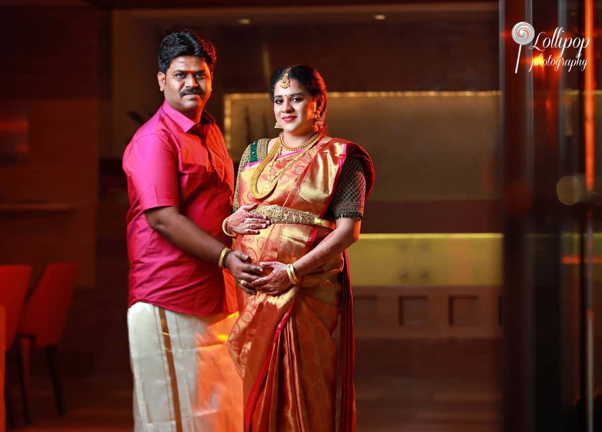 A close-bond portrait of the expecting couple, with the mother-to-be in a golden sari and the father in a bold red shirt, highlighting their connection in this special moment