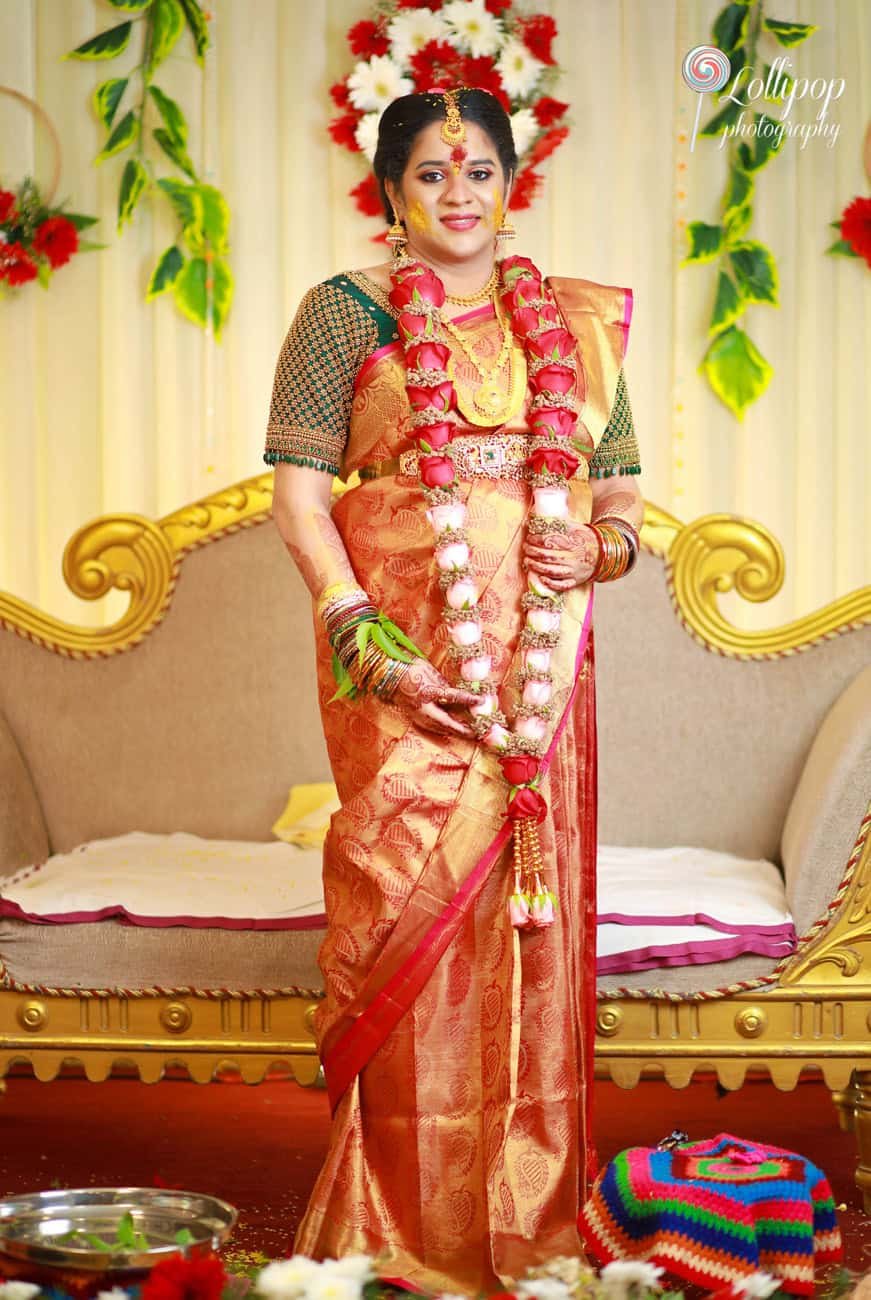 The mother-to-be adorned with a floral garland, smiling gracefully during her baby shower, captured beautifully by Lollipop Photography