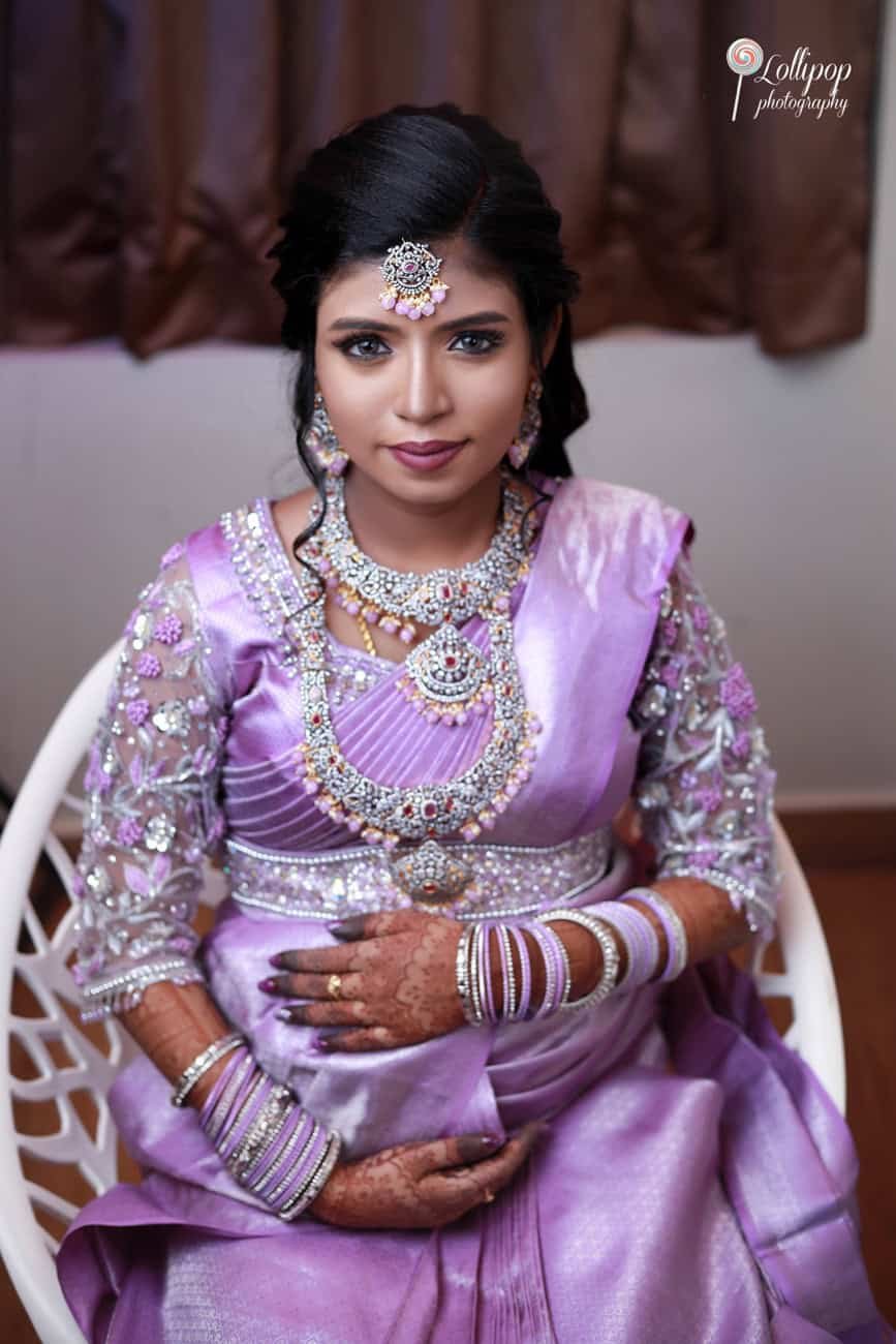 A joyful Suganthi sits with her baby bump, adorned in a lavender saree with intricate silver embellishments and traditional jewelry, radiating happiness. Captured by Lollipop Photography, Chennai