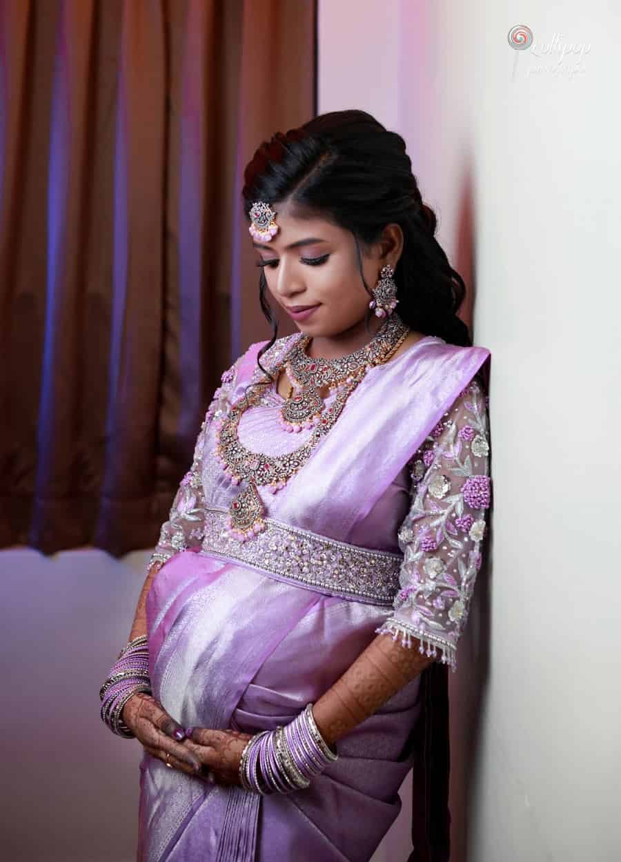 A serene side profile of Suganthi dressed in a lavender saree with detailed jewelry, softly smiling and cradling her baby bump. Captured by Lollipop Photography, Chennai